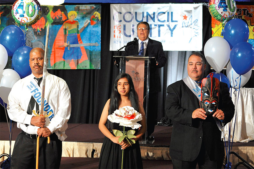 From left: Sword bearer Marc Grant, John Dewey HS student Zaineb Naseem and mask bearer James Concepcion at the Council for Unity induction ceremony, where students are celebrated for their commitment to respect, unity and making a positive impact in their schools and communities. CFU founder Bob De Sena is at the podium. Photo by Maria R. Bastone. 